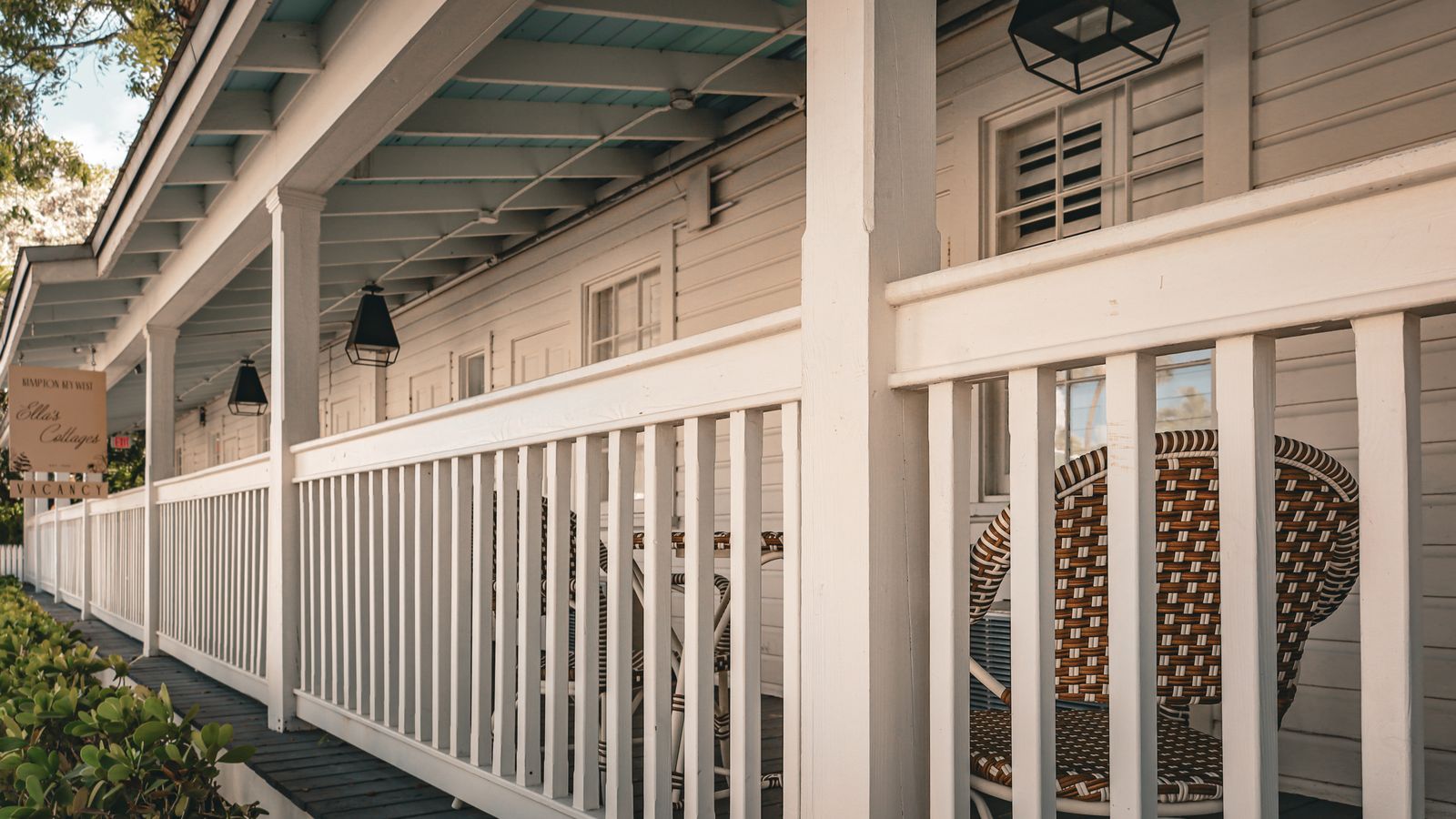 Pale haint blue porch ceiling over a white-railed Southern porch with black lantern lights and wicker chairs